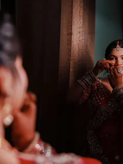 A reflection shot capturing a quiet moment of preparation. The focus is on her expressive eyes and the intricate details of her bridal jewelry.