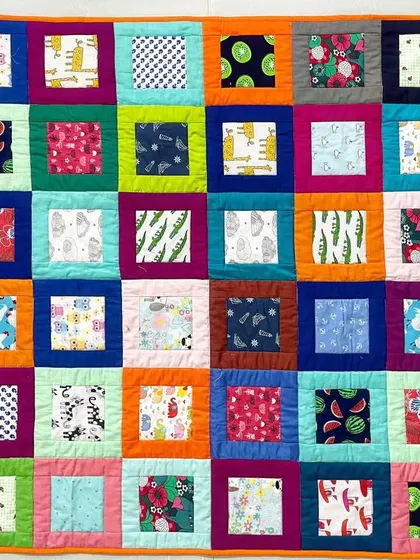 A colorful baby quilt with a "window pane" design, featuring fun prints like watermelons and giraffes.