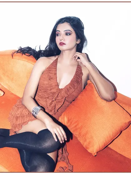 A high-fashion shot for a lookbook or campaign. The use of a vibrant orange couch and dramatic flash lighting creates a bold, retro-glam look.