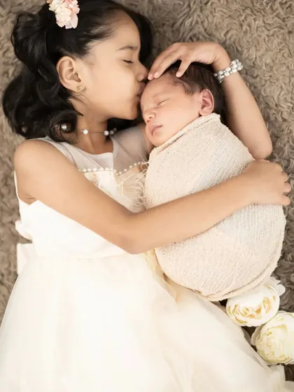The bond between siblings is so precious. This tender moment shows a big sister gently kissing her newborn sibling, a memory this family will cherish forever. We take great care during sibling and newborn photoshoots to ensure everyone is safe and comfortable.