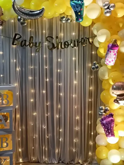 A simple baby shower decoration for a home event, featuring a yellow and silver balloon arch and 'BABY' display boxes.