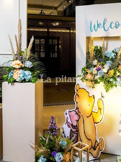 A charming welcome setup for a Winnie the Pooh party, featuring character cutouts and floral arrangements in soft, gentle colors.