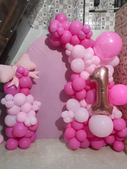 A first birthday setup featuring a pink arch backdrop framed by balloon pillars in shades of pink.