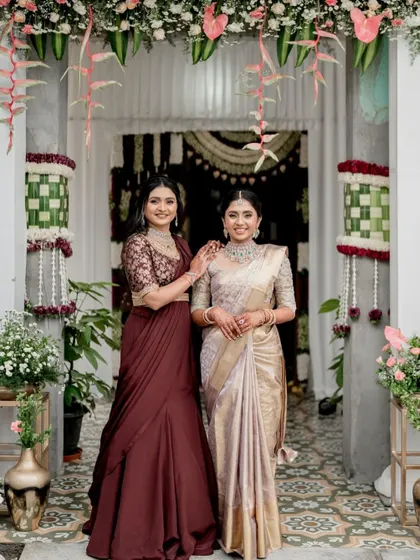 Two stunning sisters at an engagement ceremony. On the left, a custom Indo-western set with a fish-cut skirt, and on the right, a classic lavender saree with a custom embroidered blouse.