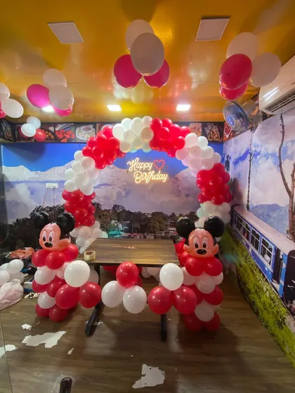 A Mickey Mouse themed birthday decoration in a restaurant with a red and white balloon arch and character sculptures.