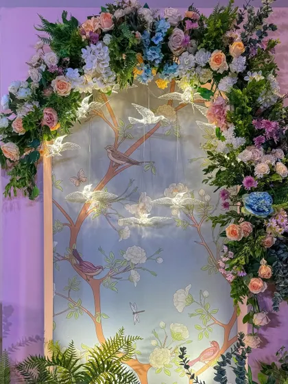 A key decor element: a custom Chinoiserie-print backdrop framed by an arch of pastel pink, peach, and ice blue flowers, with delicate bird hangings.