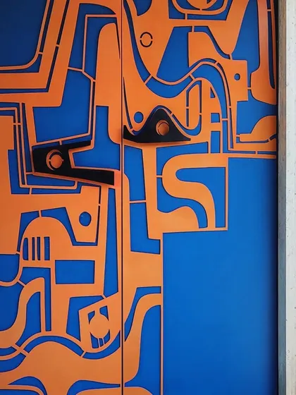 A direct, close-up shot of the abstract orange and blue door, showcasing the clean lines and bold color contrast of this piece of functional art.
