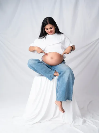 A playful solo shot. The mom-to-be is all smiles as she points to her baby bump, celebrating her pregnancy with joy and humor.