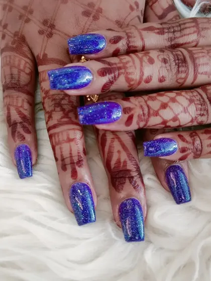 A dazzling look for a bride or special event. These square-shaped nails feature a deep blue glitter finish, beautifully contrasting with the intricate henna design.