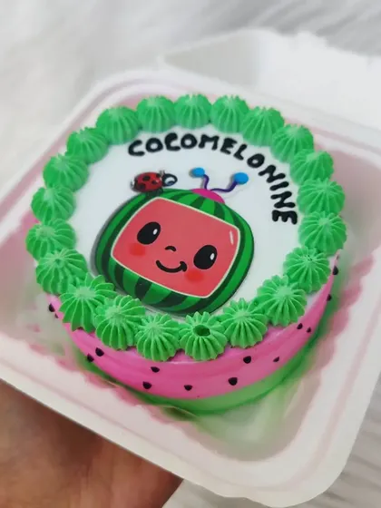 A cute Cocomelon bento cake for a 9-month celebration. The design features the iconic watermelon character with a ladybug, all done with edible prints and colorful buttercream.