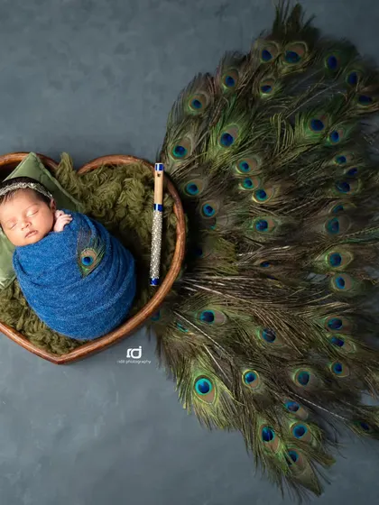 A heart-shaped arrangement of peacock feathers makes this Krishna-themed newborn photo extra special.