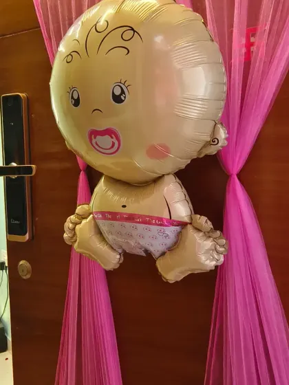 A cute baby-shaped foil balloon on a door draped with pink fabric. This is a charming and simple way to announce the arrival of a new baby.