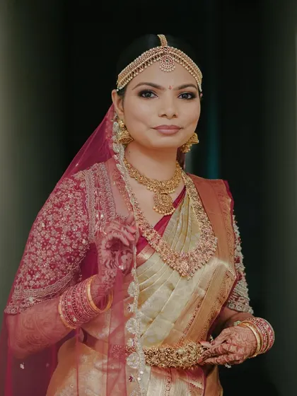 A beautiful portrait of a bride in a traditional gold Kanchivaram saree. Her custom blouse in a contrasting maroon color is heavily embroidered, creating a striking and regal look.