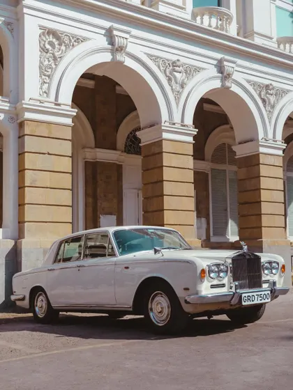 A pristine white Rolls-Royce parked in front of a grand arched building. This is the epitome of classic luxury and timeless elegance.