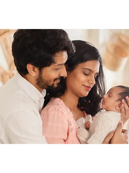 A bright and airy family portrait showing parents admiring their sleeping newborn.