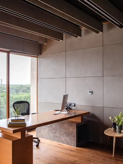 The main desk area in the MD's cabin at Anthea Pharma, with a William grey marble top and views of the surrounding greenery. The space is designed with a refined, mid-century modern feel, using a subtle color palette and acoustically optimized materials.