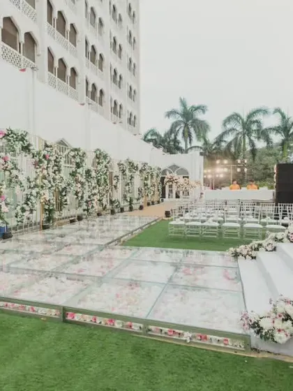 A unique setup featuring a glass floor over a bed of flowers for the guest seating area, leading to a pristine white stage.