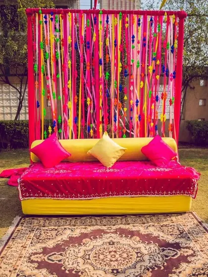 For a vibrant and fun Mehndi, I created this backdrop using a frame with colorful ribbons and tassels. The bright pink and yellow seating completes the playful look.