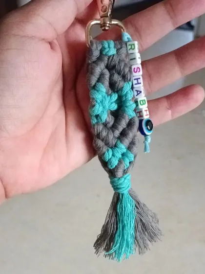 This is a close-up of a personalized macrame keychain with the name 'Rishabh'. I also added a small evil eye charm for good luck, which is a popular request.