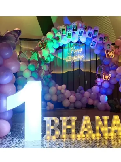 The main backdrop for Bhanavi's butterfly party, featuring a balloon ring, light-up name and number, and a photo garland of her first year.