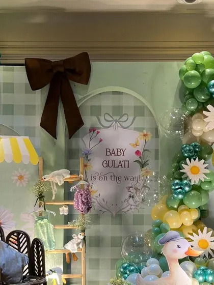 Another angle of the "Baby Gulati" backdrop, featuring a large brown bow and a beautiful balloon garland in shades of green and yellow.