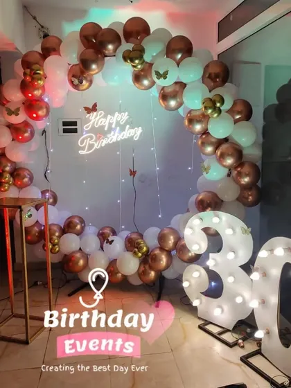 A beautiful 30th birthday setup with a white and rose gold balloon ring, accented with butterfly details and a lit-up marquee number.