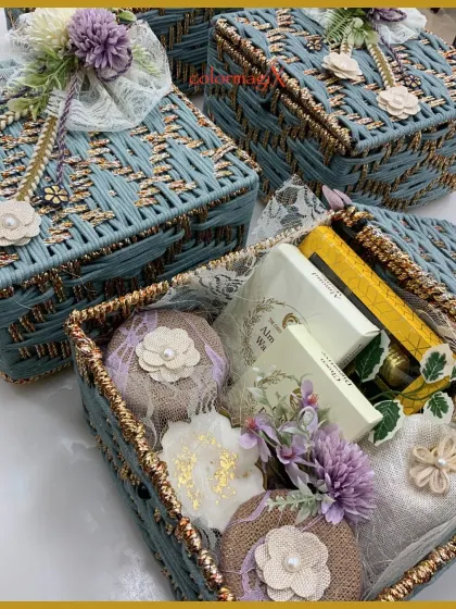 A close-up of our handcrafted blue woven baskets being filled with festive goodies. The combination of textures, from the woven basket to the lace and flowers, is visually stunning.