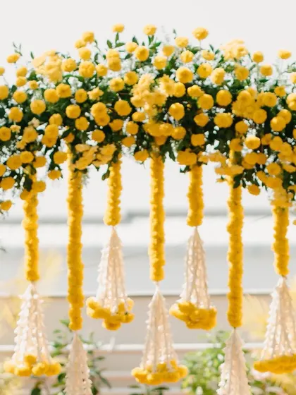 A close-up of a Haldi floral arch, showing the detail of the bright yellow flowers and traditional white tassels.