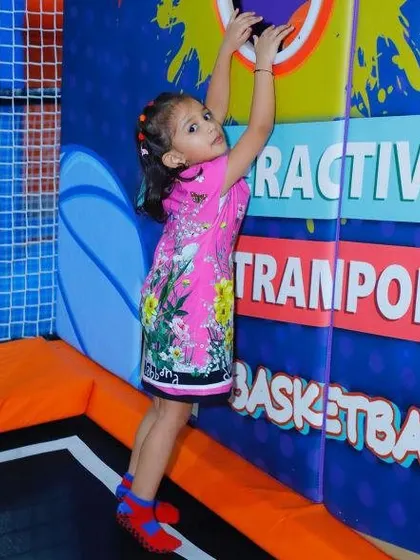 A young girl reaches for the interactive game wall, a feature that makes our trampoline park a unique and engaging experience.