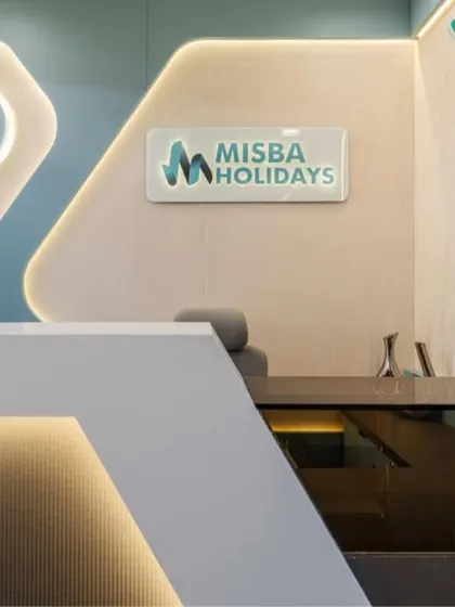 A close-up of the bespoke reception desk for Misba Holidays. The angular, minimalist design in white solid surface is accented with under-counter lighting, creating a floating effect that is both modern and welcoming.
