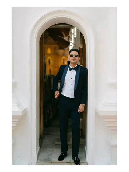 A groom in a classic tuxedo with a bow tie, looking cool and confident in a white archway. This shot is a perfect example of timeless wedding style.