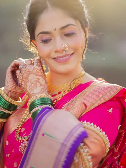 A candid moment of the bride adjusting her earring. This shot highlights the soft, shimmery eye makeup, the delicate nath, and the beautiful green glass bangles, all essential parts of the 'Marathmola' look.