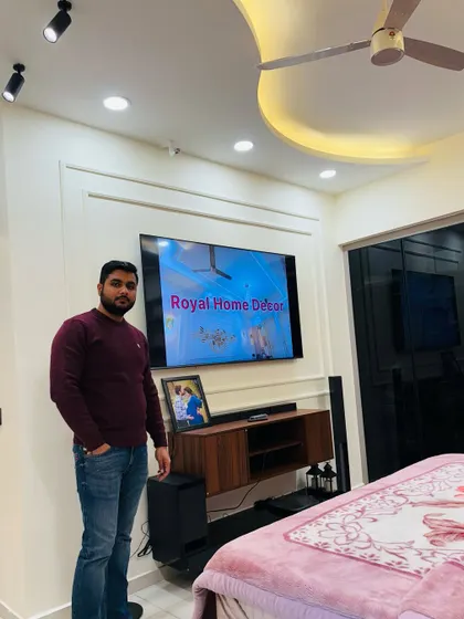 Here I am in a completed master bedroom. The design includes a simple yet elegant TV unit, a bed with a pink blanket, and a curved false ceiling that adds a modern touch.