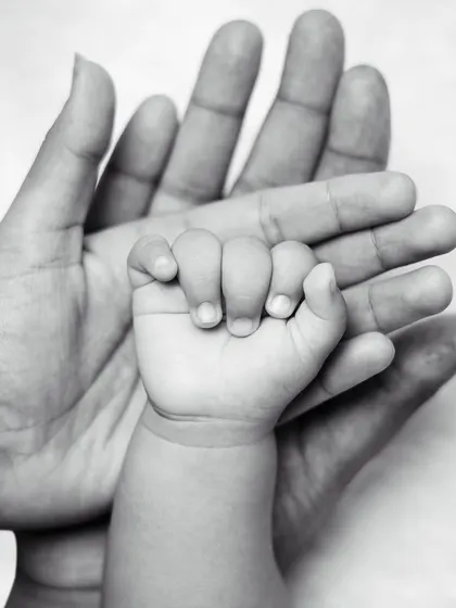 A classic black and white photo of a newborn's hand resting in their parent's palm, a beautiful symbol of their new connection.