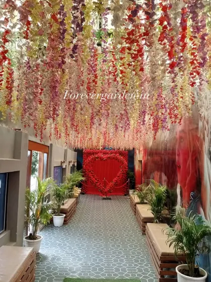 A beautiful wedding or event entrance corridor decorated with hanging wisteria flowers in multiple colors, leading to a heart-shaped floral backdrop.