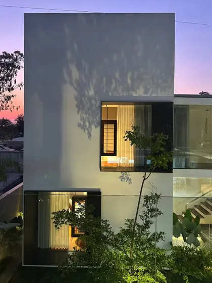 The facade of the Long House at dusk, where the interior lights create a warm glow, highlighting the interplay between solid walls and transparent glass.