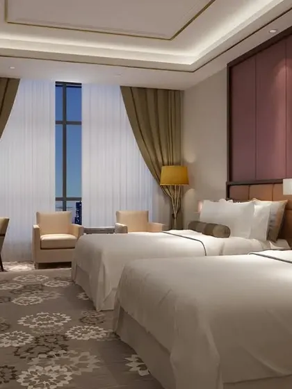 A classic and comfortable hotel-style bedroom with two beds. The design focuses on a warm color palette, plush carpeting, and functional furniture for a welcoming guest experience.