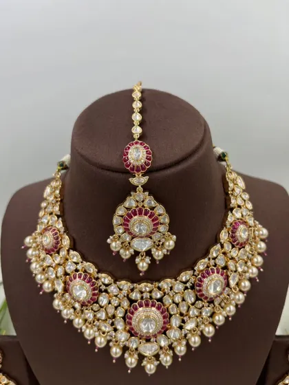 The Zarista Premium Moissanite Necklace set, shown here in both ruby and green variations. This set includes a necklace, maang tikka, and earrings, featuring large central stones surrounded by detailed craftsmanship.