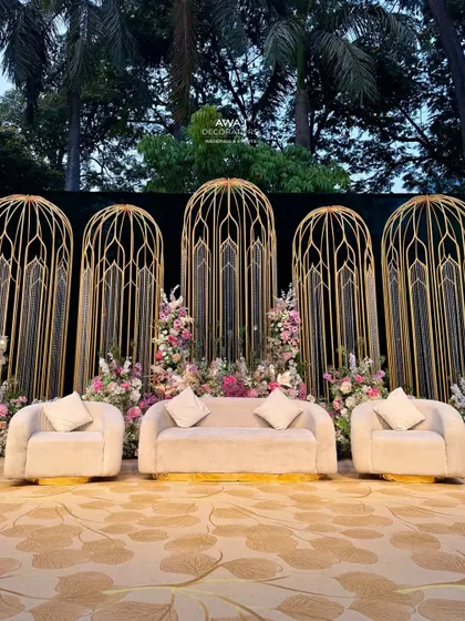A direct view of the stage, highlighting the plush cream-colored sofas set against the intricate gold backdrop and surrounded by a garden of pastel flowers.