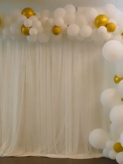 A simple and elegant balloon decoration featuring a white and gold partial arch against a white curtain. This minimalist design is perfect for sophisticated celebrations.
