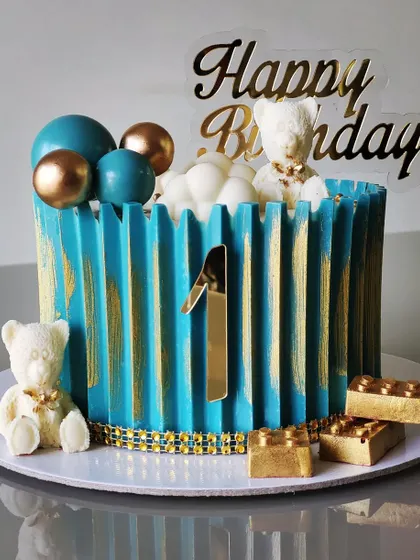 A cute and cuddly teddy bear theme for a first birthday. This cake features a modern, origami-style texture in blue and gold, decorated with edible teddy bears and building blocks.