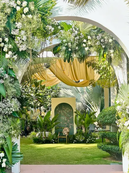 An enchanting entrance archway covered in lush greenery and white flowers, leading into a secret garden-themed celebration.