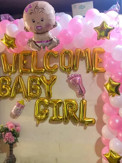 A "Welcome Baby Girl" wall decoration with a pink and white balloon arch and gold foil letters.