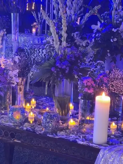 A candle-lit table at the celestial sangeet. The deep blue lighting and arrangements of purple and white flowers add to the mystical, night-time vibe of the event.