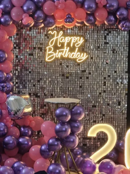 A vibrant 26th birthday decoration with a silver sequin wall framed by a pink and purple balloon arch and matching light-up numbers.