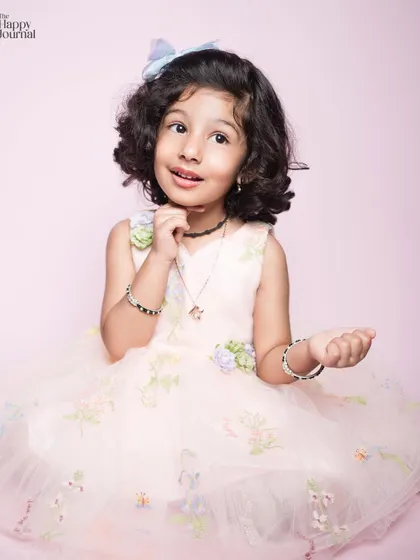 A little girl in a lovely pink dress, her expression full of curiosity and charm. The soft pink background complements her outfit perfectly.