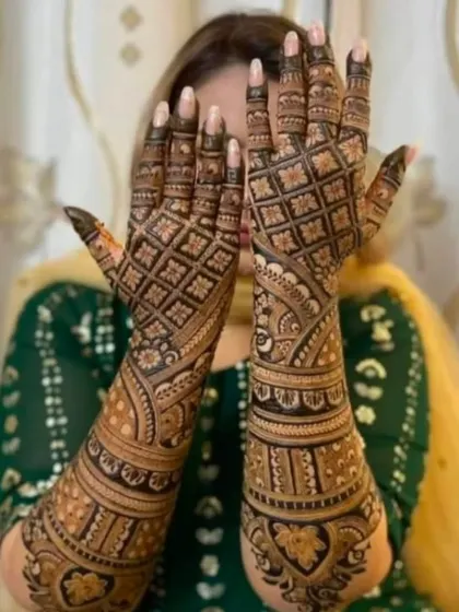A classic pose showing the back of the hands, covered in a dense checkerboard (jaali) pattern that is very popular for bridal mehandi.