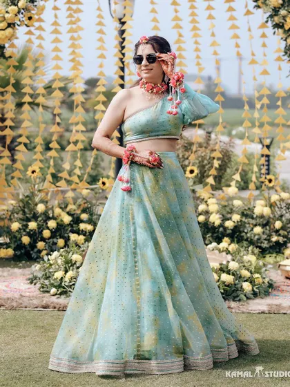 A full-length portrait of the bride in her stylish one-shoulder Haldi lehenga, looking chic and happy.
