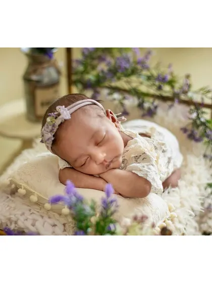 A newborn peacefully sleeping on a miniature bed surrounded by lavender flowers, creating a soft and dreamy scene.