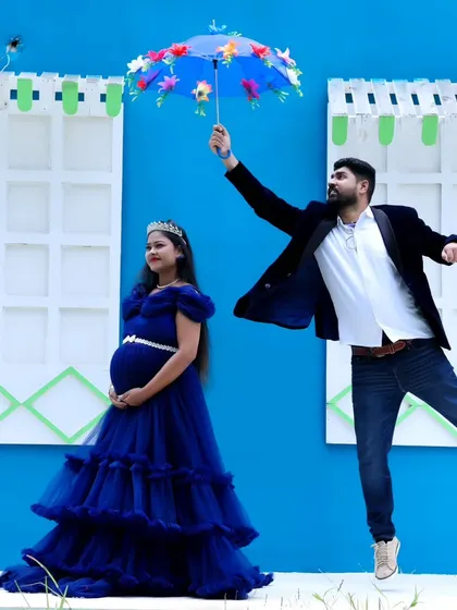 A fun and creative maternity photo, with the father-to-be seemingly floating with an umbrella next to his partner in a blue gown.